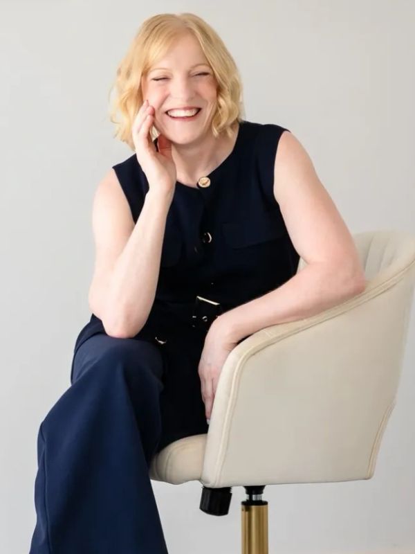 Smiling woman with blonde hair sitting on a cream swivel chair.