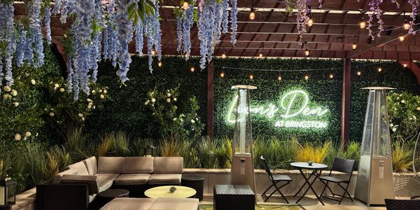 Cozy outdoor seating area with hanging flowers and heaters.