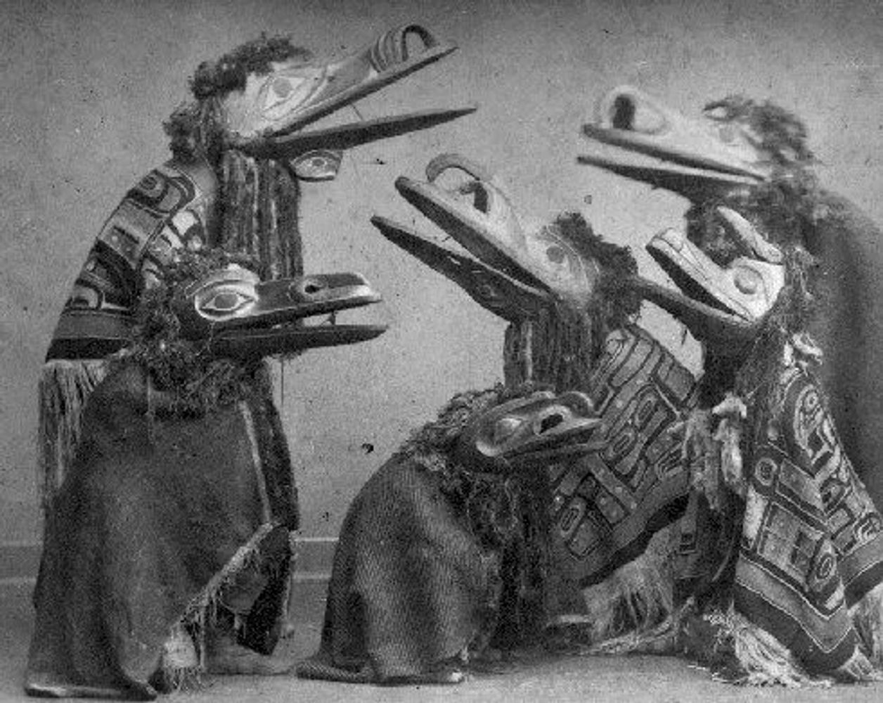 Group of people wearing traditional bird masks and patterned cloaks.