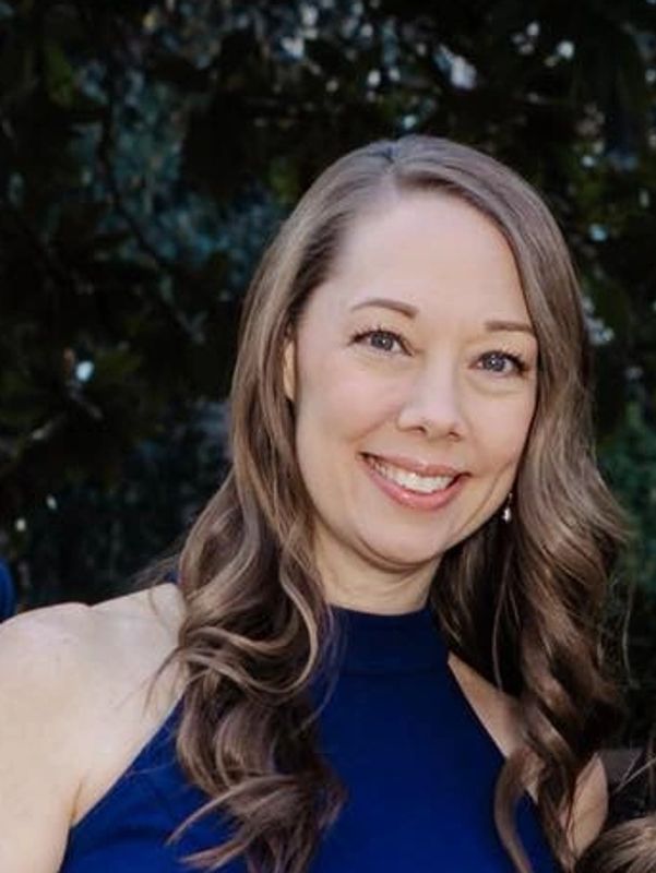 Smiling woman with wavy hair in a blue sleeveless top.
