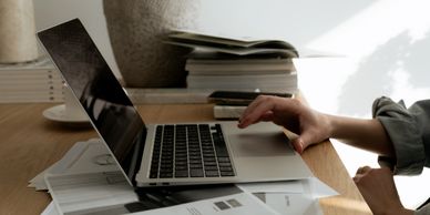 Person using a laptop on a wooden desk with papers and books.