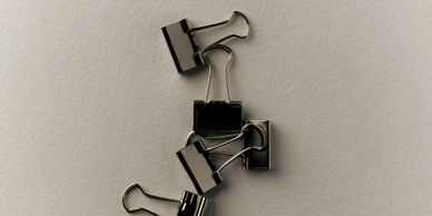 A group of black binder clips on a gray textured surface.