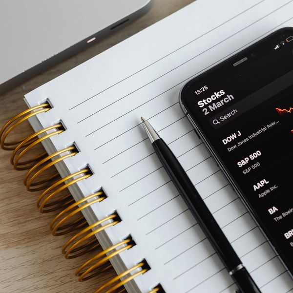 Smartphone displays stock market losses on a notebook beside a pen.