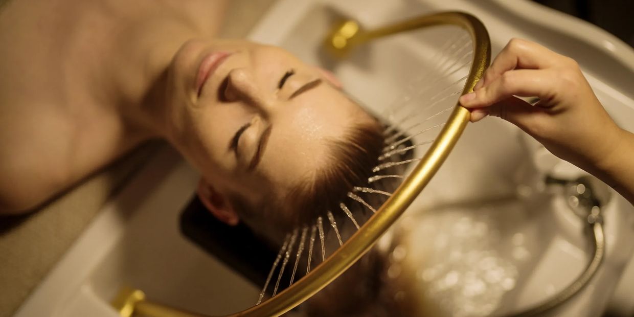 Woman enjoying a relaxing hair wash with a unique golden shower head.