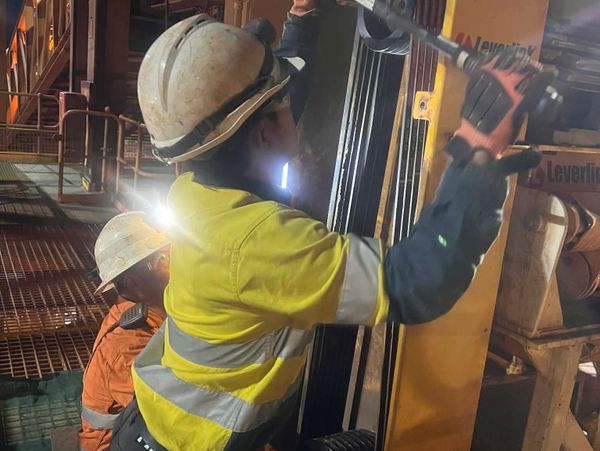 Two construction workers wearing safety gear operate heavy machinery indoors.