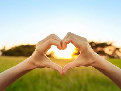 Hands forming a heart shape with the sunset in the background.