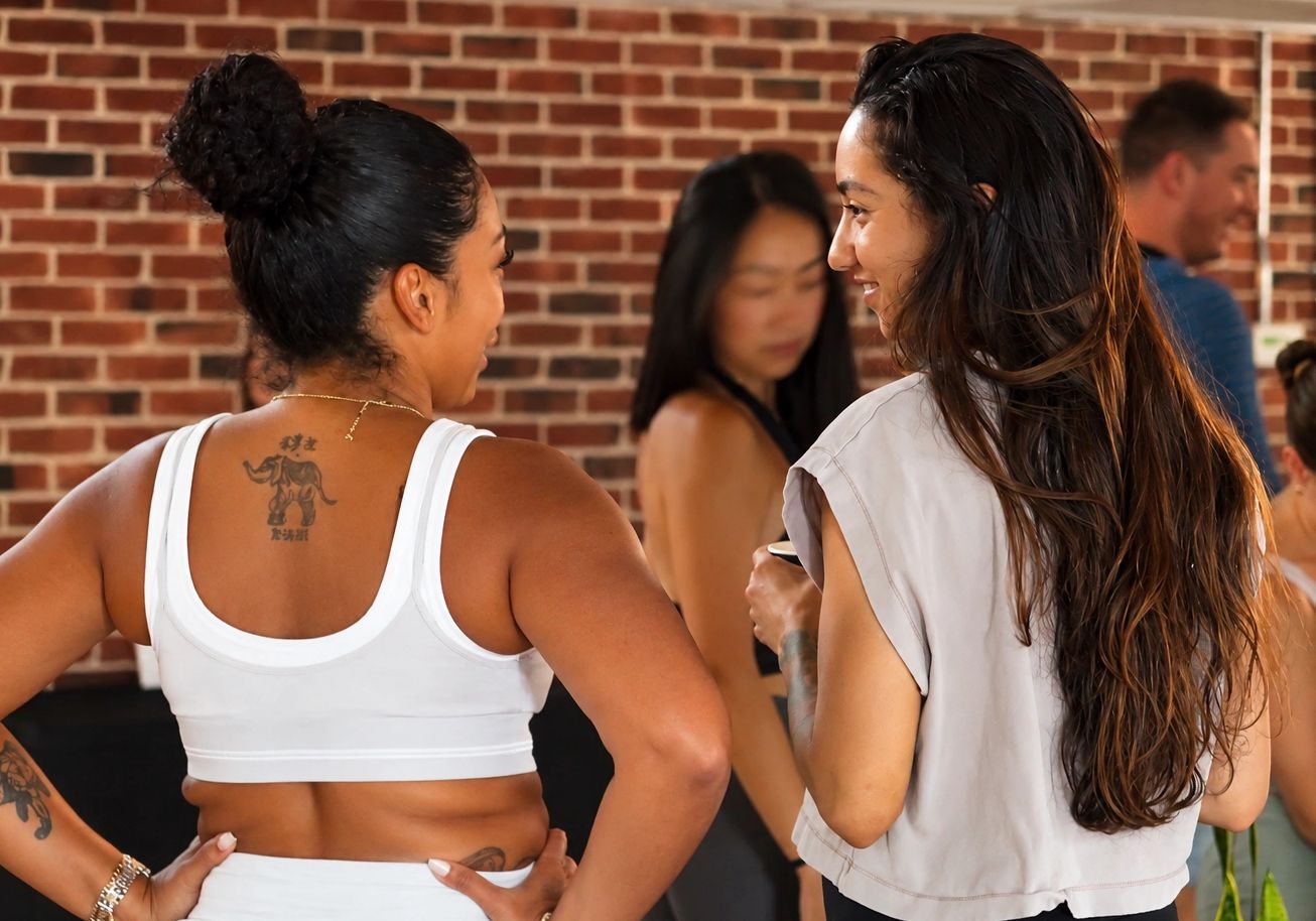 Two women chatting in a fitness setting with brick wall background.