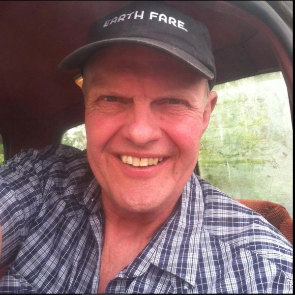 Man smiling in a checkered shirt and a black cap.