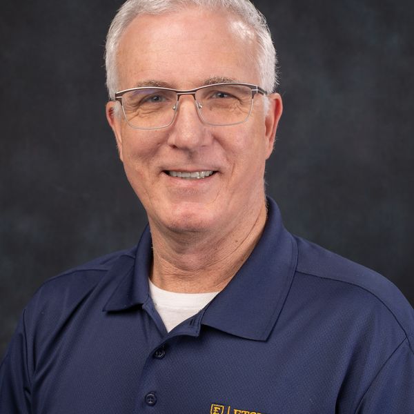 Smiling older man with glasses in a navy collared shirt.
