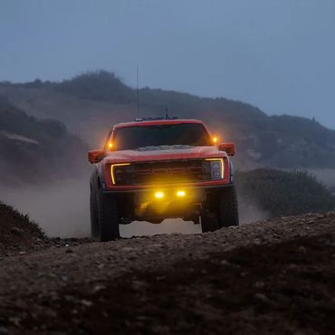 Red off-road truck with bright yellow lights driving on a dusty trail.