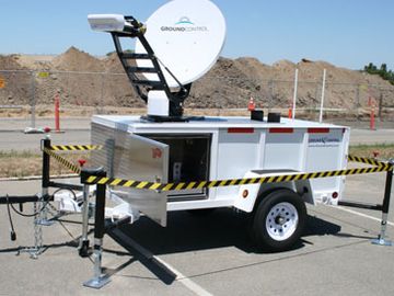 A mobile ground control unit with a satellite dish set up in a parking lot.