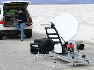 Man working on laptop near satellite communication equipment in a remote area.