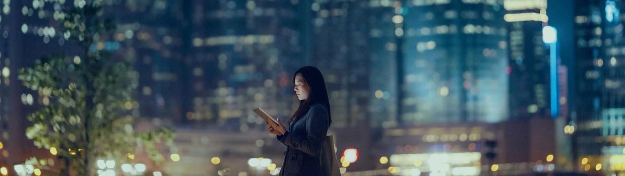 Woman reading a tablet in a city at night with blurred lights.