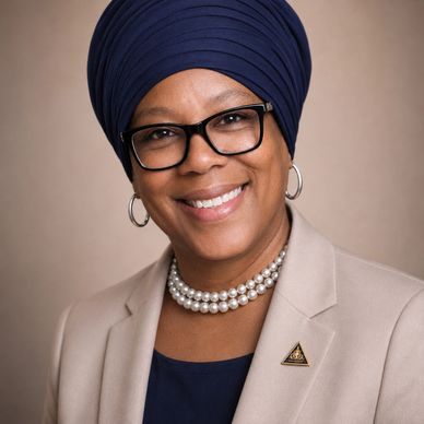 Confident woman wearing glasses, a navy turban, and pearls smiles warmly.