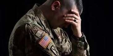 A soldier in uniform sitting with his head in his hand, looking distressed.
