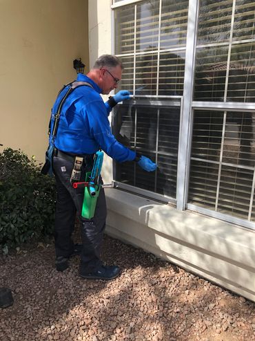 Man wearing gloves stands in front of a large residential window and removes a window screen