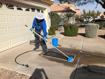 Man stands in drive way and uses long scrub brush on pie to scrub a window screen with soap & water