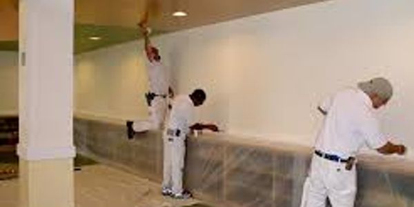 Three workers painting a wall indoors.