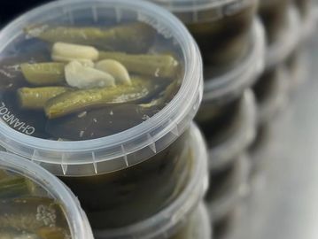 Stacked plastic containers filled with pickled vegetables and garlic cloves.