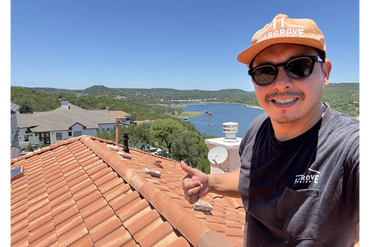 Man giving thumbs up on a rooftop with a lake and hills in the background.
