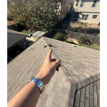 Hand pointing to damaged roof shingles on a sunny day.