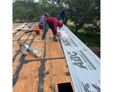 Three workers install roofing underlayment on a wooden roof deck.