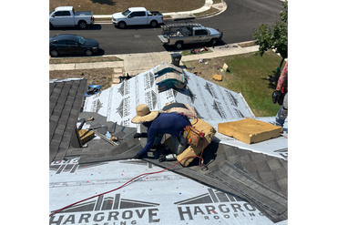 A roofer installing shingles on a residential roof under sunny weather.