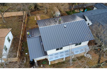 Two workers install a modern metal roof on a house under construction.