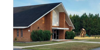 Brick building with a playground and green bushes outside on a sunny day.