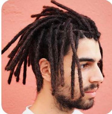 Profile of a man with thick, styled dreadlocks against a pink wall.