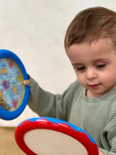 A toddler playing with colorful tambourines, focused on the activity.