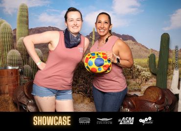 Two smiling women posing in matching pink tops with a desert cactus backdrop.