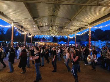People enjoying a lively evening dance event under string lights in an open pavilion.