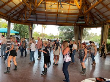 Group of people line dancing in a covered outdoor pavilion.