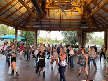 Group of people line dancing in a covered outdoor pavilion.