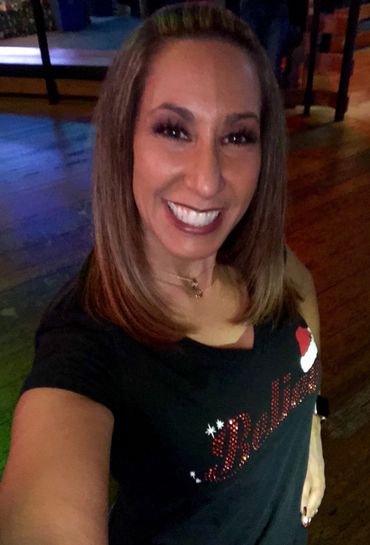 Smiling woman wearing a festive holiday shirt with a Santa hat design.
