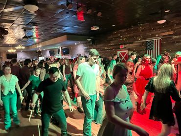 A large group of people line dancing in a dimly lit venue with American flag.