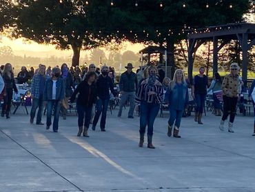 Group of people dancing outdoors in the evening under string lights.