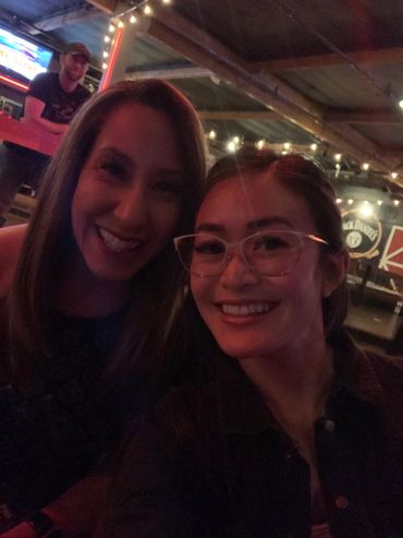 Two women smiling for a selfie in a warmly lit bar.