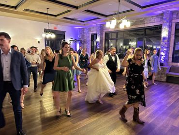 Wedding guests and bride enjoying a group dance in a warmly lit venue.
