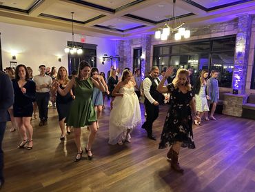 A group dancing at a wedding reception in a warmly lit room.