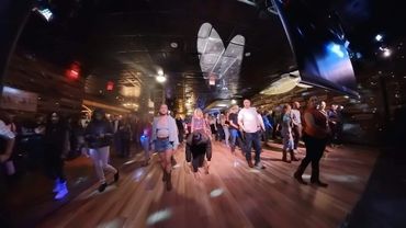 Group of people line dancing in a dimly lit venue with wooden floors.