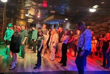 Group of people lined up on a wooden floor in colorful lighting.
