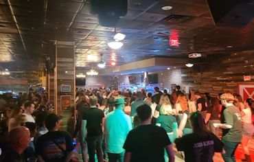 Crowded indoor venue with people socializing and dancing under warm lighting.