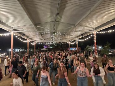 Large group dancing together under a decorated pavilion at night.