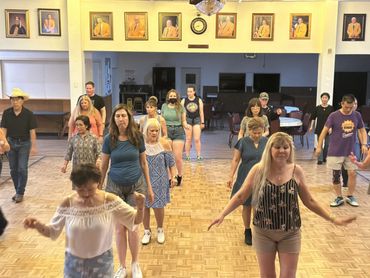 A diverse group of people practicing line dancing in a hall.