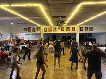 Group line dancing in a decorated community hall with framed portraits.