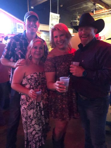 Four friends enjoying drinks and smiling at a lively indoor event.