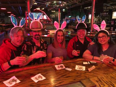 Five friends wearing bunny ears hats enjoy drinks together at a bar.