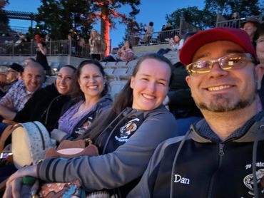 A group of friends smiling and enjoying an outdoor event in the evening.